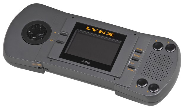 The original Atari Lynx, a large grey handheld with a backlit colour screen and controls on both sides.