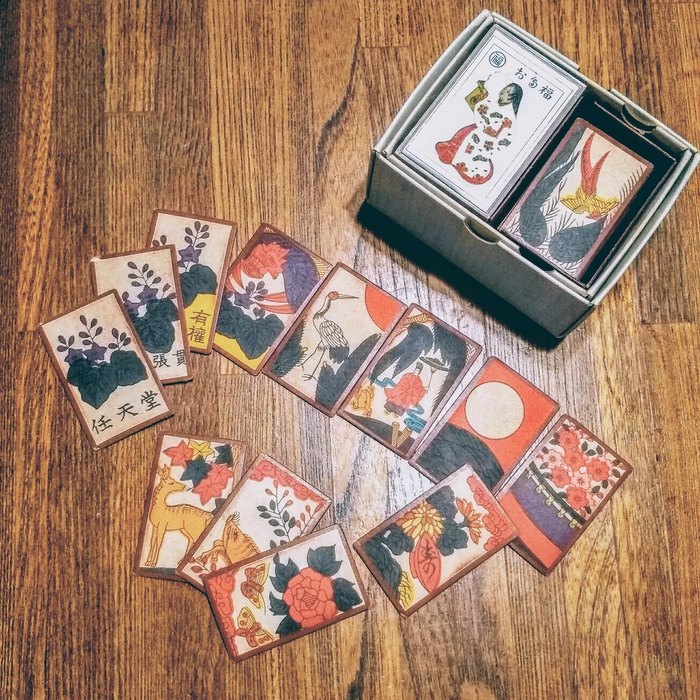 A box of Nintendo hanafuda playing cards with a dozen cards fanned out on a wooden table, showing painted flowers, a crane and a deer.