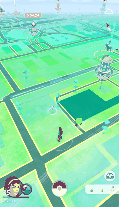 Pokémon Go on a phone: an overhead map of green fields and roads with the player avatar in the middle, Poké Stops dotted around, a gym tower on the right and a Poké Ball button at the bottom.