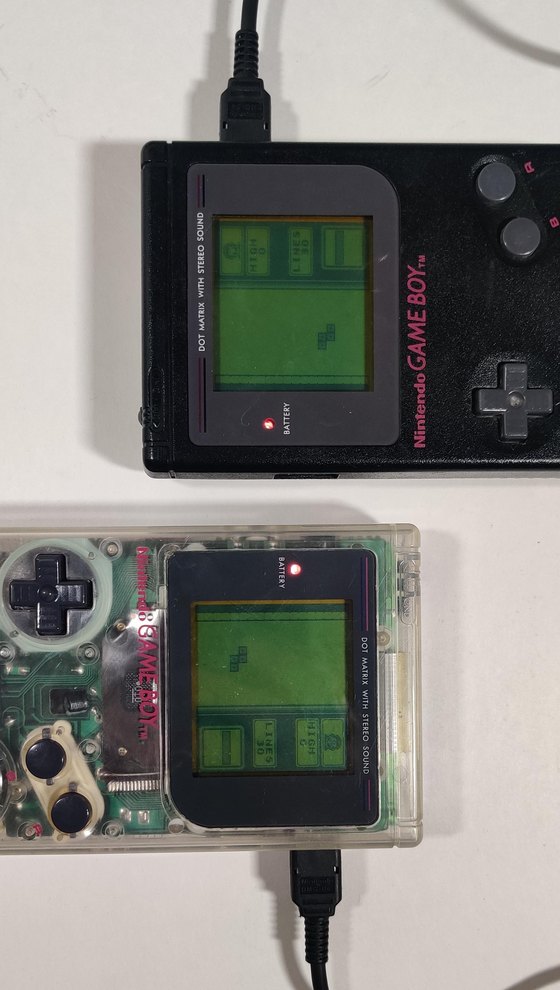 Two original Game Boys, one black and one transparent, joined by a link cable and both running two-player Tetris.