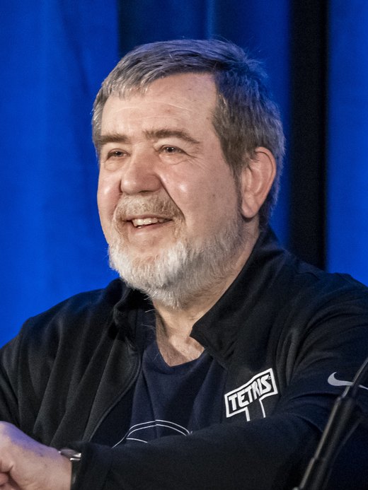 Alexey Pajitnov, grey-haired and bearded, smiling in a black Tetris-branded jacket.