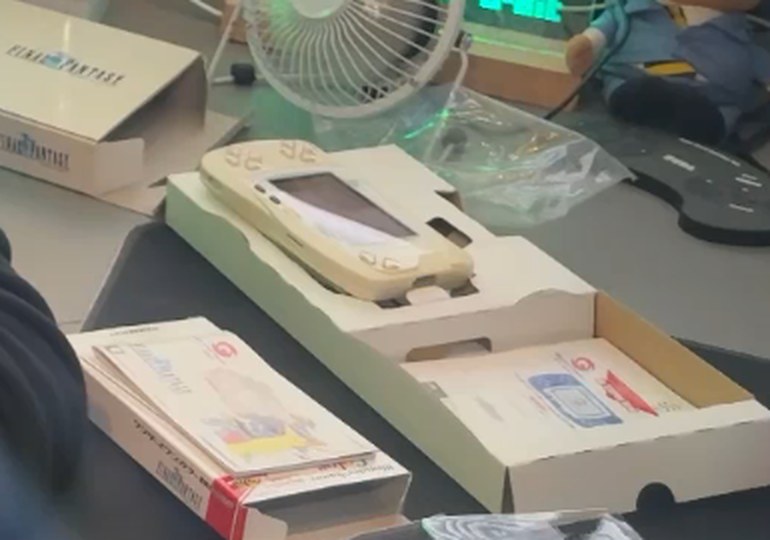 A pearl white WonderSwan Color sitting in its cardboard inner tray, with the Final Fantasy outer sleeve behind it and a Japanese manual alongside.